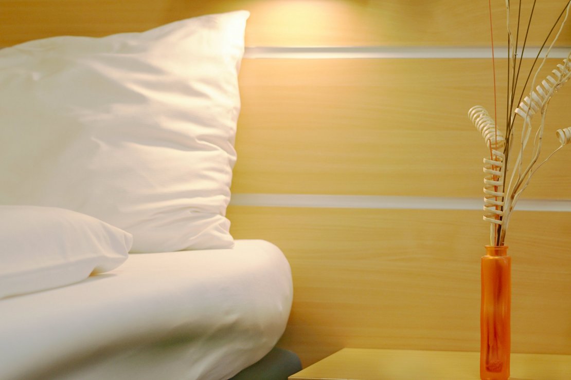 Bett mit Nachtkästchen, auf dem eine kleine Vase steht